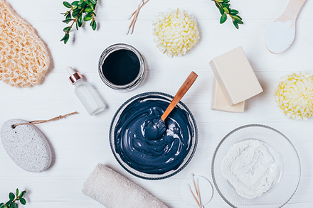 A photo of a thoughtfully-placed slew of ingredients that look like skincare and vary from herbs to a loofa to serum to a bowl of blue goo. 