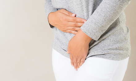 Woman presses her hands to her stomach & crotch area, indicating pain in the urogenital region.