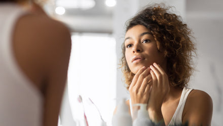 Woman looking in mirror appears to be picking or squeezing her pimples.