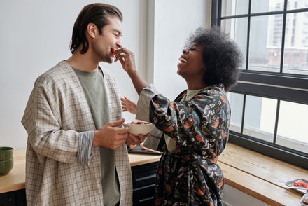 A happy, heterosexual couple laughs as they feed each other something from a bowl